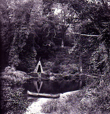 black and white photo of teepee and canoe on shore of lake